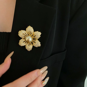 Detail of a gold floral brooch with pearl center and zircon petals on a black blazer