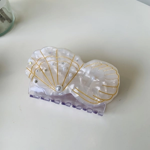 Detail of a pearl white shell hair claw clip with golden accents and small rhinestones