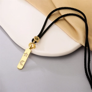 Pendentif étoile lune doré sur cordon noir avec détail gemme verte sur plateau blanc