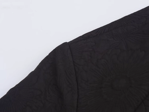 Close-up of black floral embossed jacquard fabric and stitching on a jacket shoulder