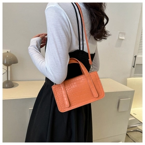 Orange croc-effect handbag worn by model against a minimalist home background