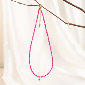 Detail of bohemian rose red beaded necklace with gold heart charm on a branch