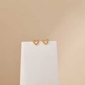 Macro detail of gold-plated heart stud earrings with micro-pave cubic zirconia on a white stand