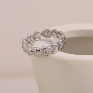 Macro shot of silver heart-shaped beaded ring leaning on beige ceramic pottery edge