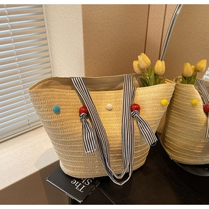 Detail of hand-woven straw tote with colorful pom-poms and striped handles for beach vacations