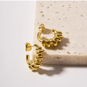 Macro shot of gold spiral twist hoop earrings on a textured stone display platform