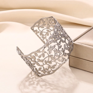 Detail view of silver hollowed leaf pattern wide open bangle on a beige jewelry display