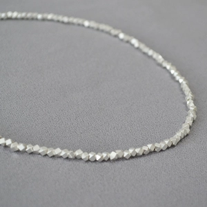Macro detail of irregular faceted silver beads on a minimalist brass gold necklace