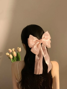 Large pink satin bow hair clip with long ribbons shown on model's head from behind