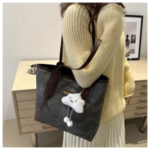 Detail of grey tote bag with leather trim and a white cloud plush charm in a lifestyle setting
