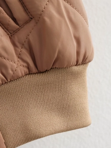 Detailed close-up of khaki quilted bomber jacket featuring ribbed knit hem and texture