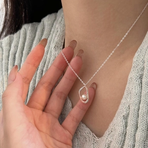 Detailed view of irregular silver pendant with pearl on soft knit fabric background