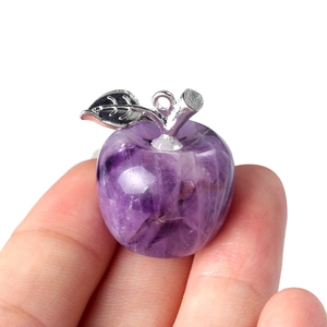 Natural purple crystal apple pendant with silver leaf held in hand against white background