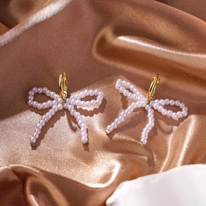 Close-up of elegant gold bow earrings with white micro pearls on bronze silk fabric