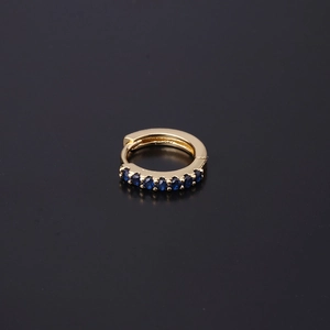 Detailed close-up of golden huggie earring with deep blue cubic zirconia stones
