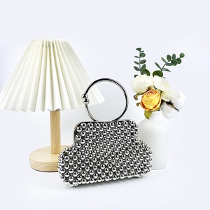 Detail of silver beaded handmade clutch bag with round metal handle on elegant desk