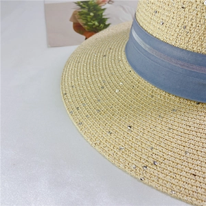 Close-up of beige straw sun hat with blue ribbon and shimmering silver sequins detail