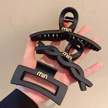 Detailed view of three matte black BB hair clips with gold logo held in hand