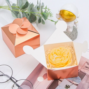 Rose gold petal-top gift box with flower candle and raffia filler on white background