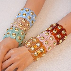 Macro view of acrylic resin bracelets with gold studded accents on textured background