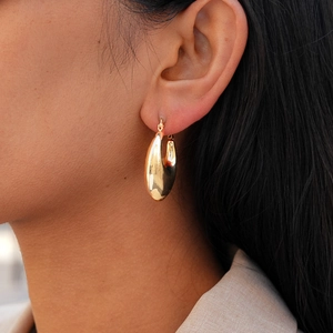 Close-up of chunky gold-tone teardrop hoop earrings worn by a model in a minimal setting