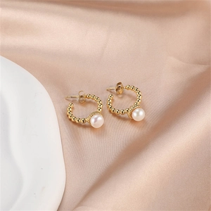 Close-up of golden beaded hoop earrings with white pearls on silk fabric