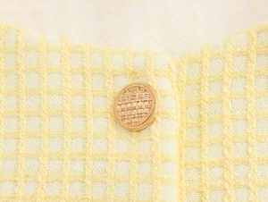 Detail of a vintage golden round button on pale yellow tweed fabric showing fine texture