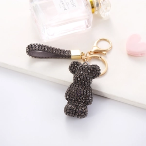 Detail of grey rhinestone-encrusted bear keychain with a sparkling woven strap and gold clasp