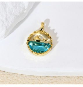 Detail of gold dolphin pendant with blue crystal on a natural textured stone surface