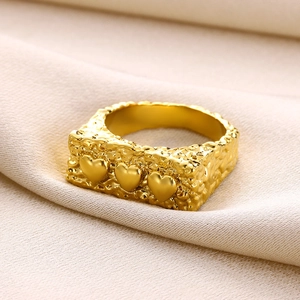 Close-up of golden irregular textured ring band with three dimensional heart charms