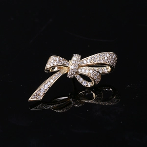 Macro shot of gold bow brooch with micro-pave cubic zirconia on reflective black surface