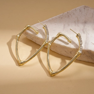 Close-up of golden bamboo-style earrings with sparkling diamonds on a stone surface