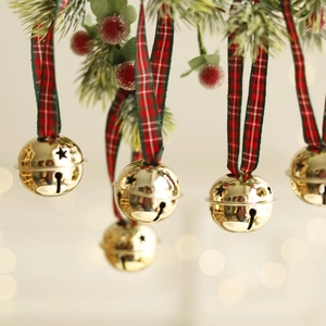 Golden Christmas bells with red plaid ribbons hanging on a pine tree branch
