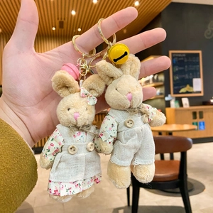 Cute plush bunny keychains in floral outfits held by hand against warm shop background
