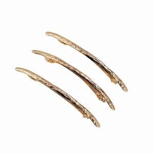 Three long gold metal hair clips with irregular hammered texture on white background