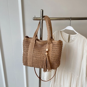 Handcrafted straw tote bag in khaki with beaded tassels and a white dress backdrop