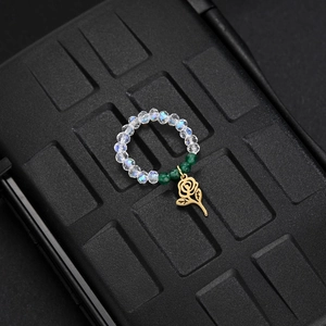 Macro shot of elastic beaded ring with green crystal beads and rose metal charm