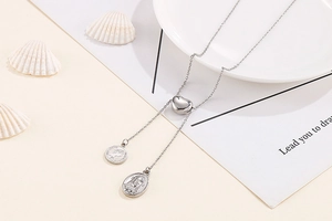 Detail of silver Y-shaped chain necklace with heart slider and coin pendants