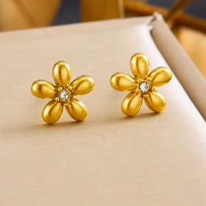 Gold-plated floral stud earrings set with zircon center on a beige jewelry display