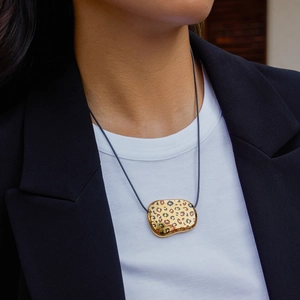 Detail of gold leopard print bean pendant on a black cord necklace worn by a model
