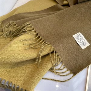 Detailed close-up of soft bicolor wool scarf texture with fringes and beige fabric label