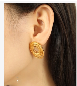 Close-up of a woman wearing gold spiral hoop earrings made of polished titanium steel