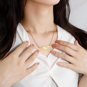 Detail shot of a minimalist gold feather pendant necklace worn by a female model