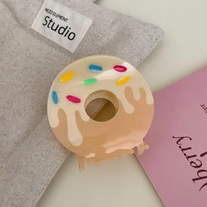 Close-up of beige donut-shaped hair claw clip with colorful sprinkles on fabric