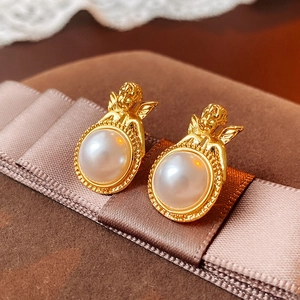 Dettaglio ravvicinato di orecchini vintage a forma di angelo d'oro con grandi perle