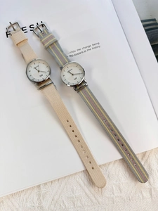 Detail of two beige and checkered nylon strap quartz watches on a minimalist book