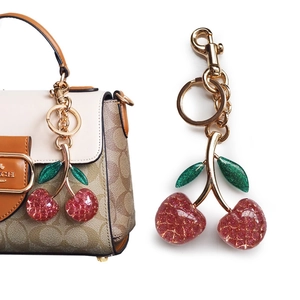 Detail of cherry keychain with pink glitter finish and golden chain on a handbag