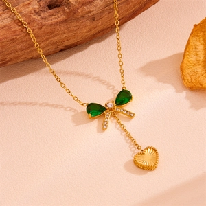 Set collana dorata con fiocco di smeraldo e ciondolo a cuore su sfondo naturale