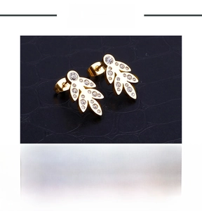 Macro shot of gold leaf earrings with small white zircons on textured black background