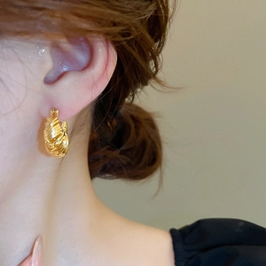 Close-up of a gold-plated U-shaped earring with twisted texture worn by a model